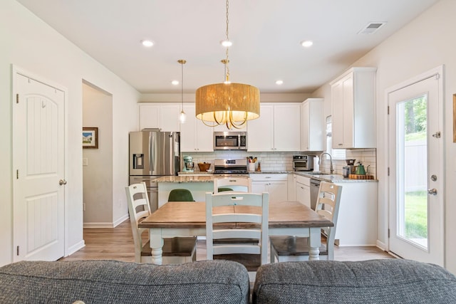kitchen featuring a kitchen island, backsplash, appliances with stainless steel finishes, a sink, and light wood-style floors