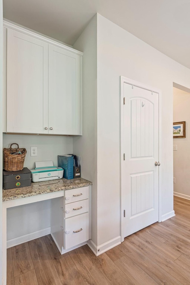office featuring baseboards, light wood-style flooring, and built in desk