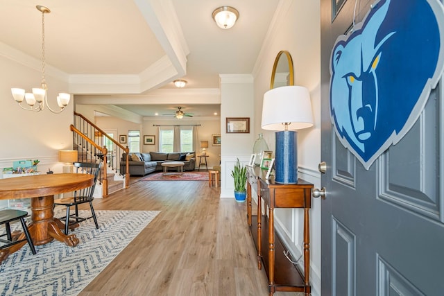 entrance foyer with wainscoting, light wood-type flooring, ceiling fan with notable chandelier, ornamental molding, and stairs