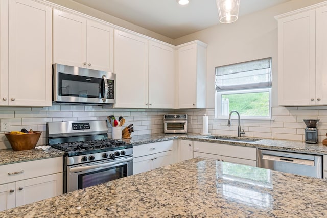 kitchen with white cabinets, light stone countertops, a sink, stainless steel appliances, and tasteful backsplash