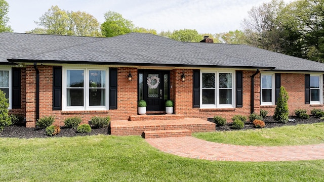 ranch-style home with brick siding, a front yard, a chimney, and roof with shingles