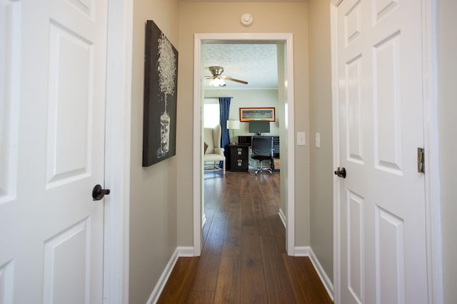 hall with dark wood-style flooring, baseboards, and a textured ceiling