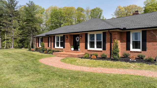 ranch-style home with roof with shingles, a chimney, a front yard, and brick siding