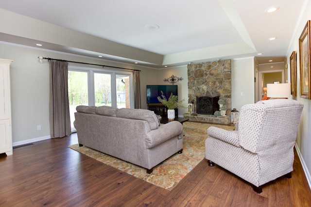 living room with recessed lighting, a raised ceiling, dark wood-style flooring, and a stone fireplace
