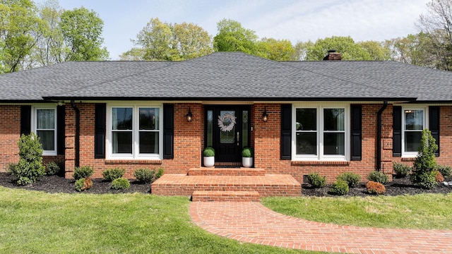 single story home featuring brick siding, a front lawn, roof with shingles, and a chimney