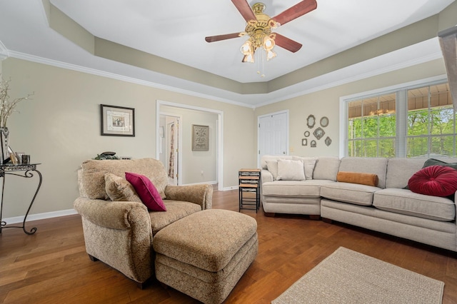 living area with ceiling fan, wood finished floors, baseboards, ornamental molding, and a tray ceiling