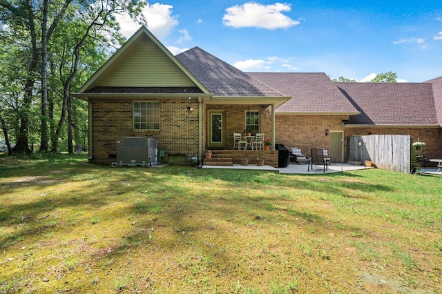 back of property with a lawn, brick siding, a shingled roof, and a patio area