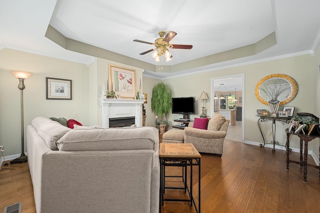 living area featuring ceiling fan, visible vents, dark wood finished floors, a raised ceiling, and baseboards