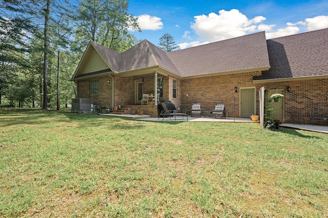 back of house featuring roof with shingles, a lawn, brick siding, an outdoor hangout area, and a patio