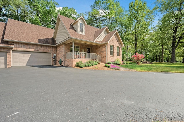 view of front facade featuring covered porch, brick siding, a shingled roof, an attached garage, and driveway