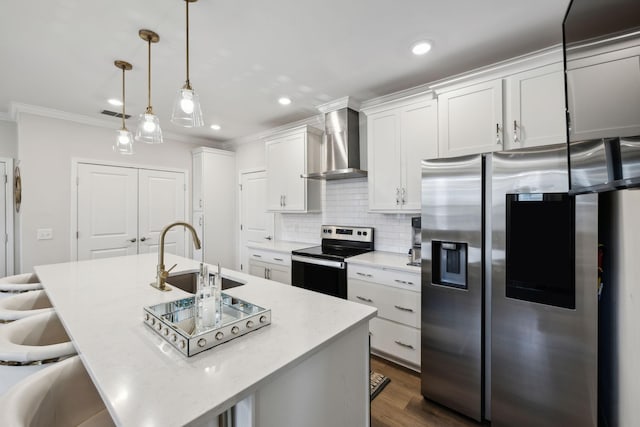 kitchen featuring a sink, wall chimney exhaust hood, a center island with sink, stainless steel appliances, and ornamental molding