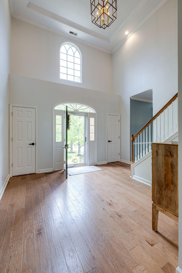 foyer entrance with a high ceiling, wood-type flooring, a healthy amount of sunlight, visible vents, and stairway