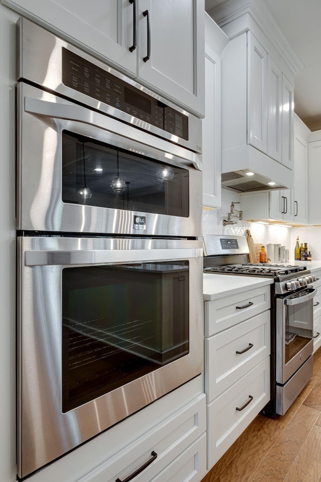 kitchen with light wood-type flooring, custom range hood, light countertops, white cabinets, and stainless steel appliances