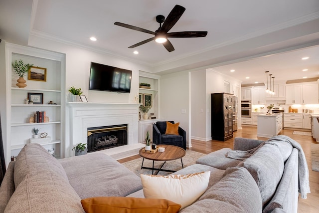 living area featuring crown molding, a fireplace with raised hearth, a ceiling fan, recessed lighting, and light wood-type flooring