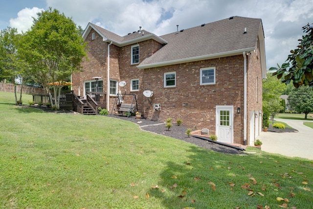 rear view of house with driveway, a lawn, a deck, brick siding, and a shingled roof