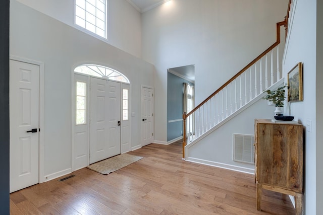 entrance foyer with light wood-style floors, a high ceiling, stairway, and visible vents