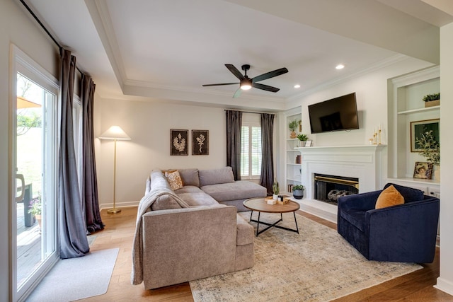 living room featuring a healthy amount of sunlight, light wood-style floors, ornamental molding, and a fireplace with raised hearth