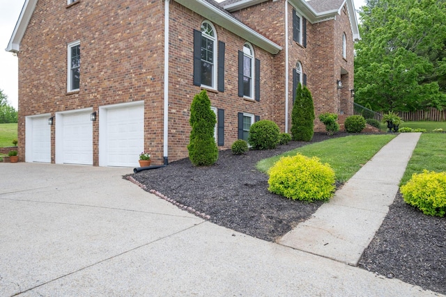 view of side of home featuring a lawn, fence, brick siding, an attached garage, and driveway