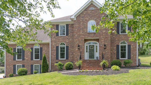 view of front of home featuring brick siding, entry steps, a front yard, and roof with shingles