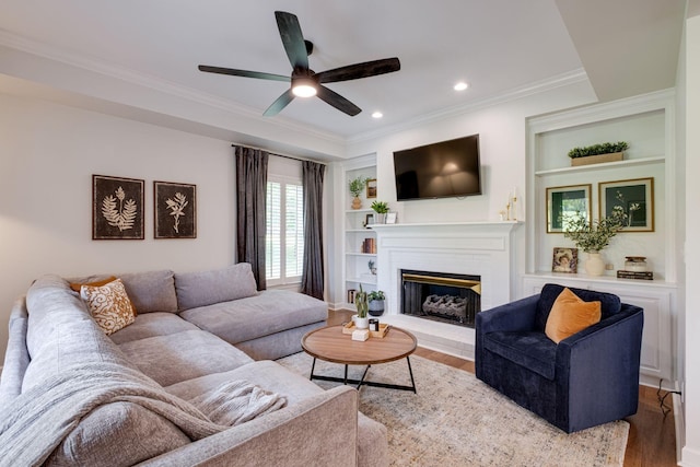 living area featuring ceiling fan, ornamental molding, a brick fireplace, and wood finished floors