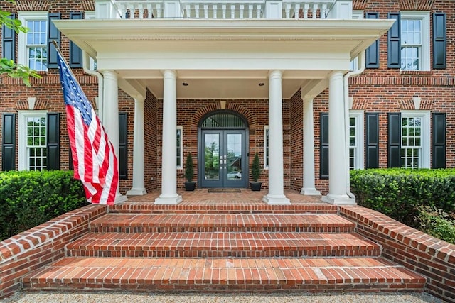 entrance to property featuring covered porch, brick siding, and french doors