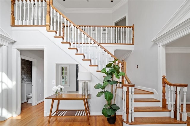 staircase with baseboards, ornamental molding, a towering ceiling, and wood finished floors