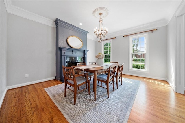 dining room featuring crown molding, a premium fireplace, a chandelier, baseboards, and wood finished floors