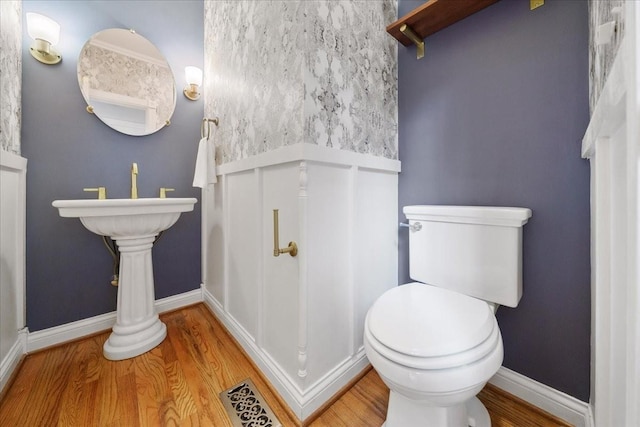 half bathroom featuring visible vents, baseboards, wood finished floors, and toilet