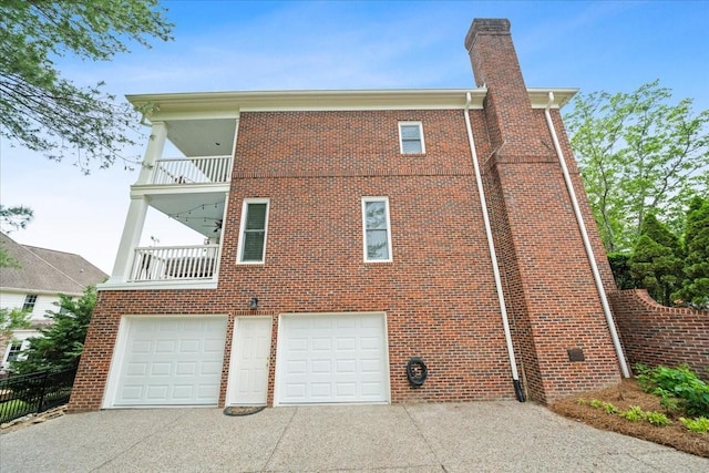 view of home's exterior featuring brick siding, a garage, a balcony, and concrete driveway