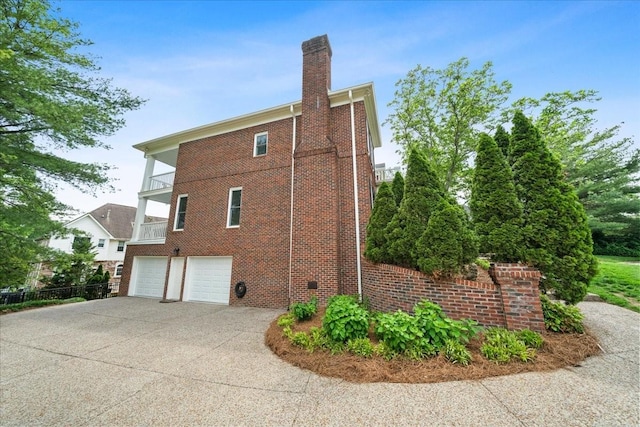 view of side of home featuring an attached garage, brick siding, driveway, and a chimney