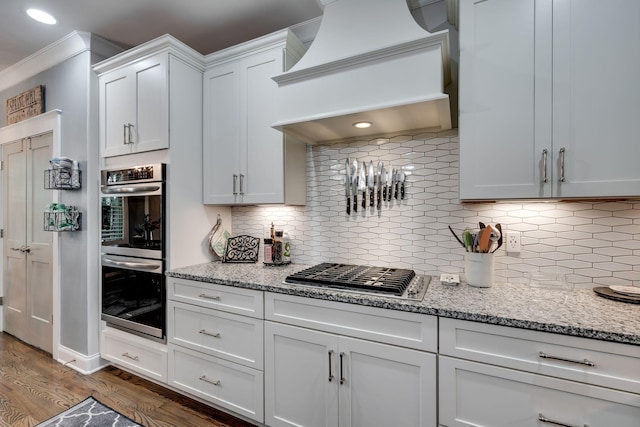 2965 Stewart Campbell Pt, Spring Hill, TN 37174 - kitchen featuring dark wood-style flooring, appliances with stainless steel finishes, tasteful backsplash, light stone countertops, and premium range hood