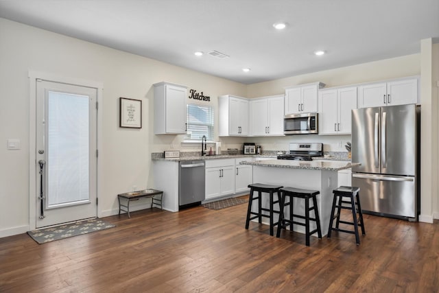 kitchen featuring a breakfast bar, a center island, white cabinetry, light stone counters, and stainless steel appliances