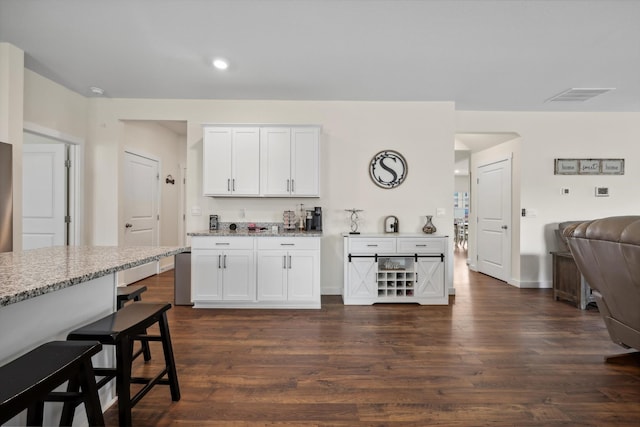 kitchen featuring light stone counters, a breakfast bar area, dark wood finished floors, white cabinetry, and visible vents