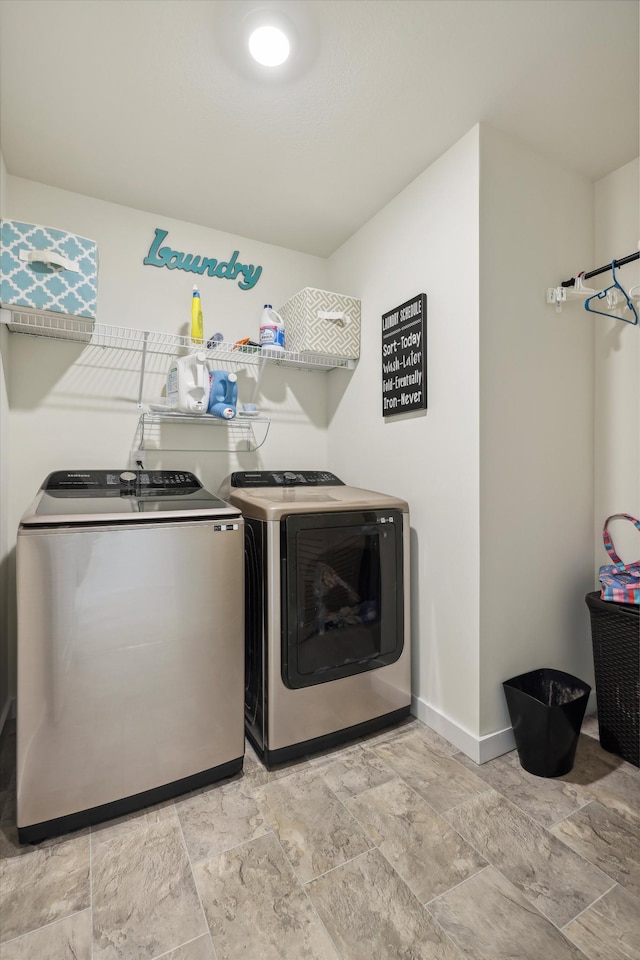 clothes washing area featuring baseboards, laundry area, stone finish flooring, and washer and clothes dryer