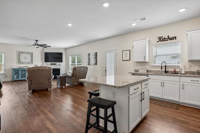 kitchen with visible vents, a center island, white cabinetry, a sink, and dark wood finished floors