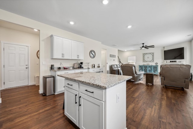 kitchen featuring light stone counters, open floor plan, ceiling fan, and dark wood-type flooring
