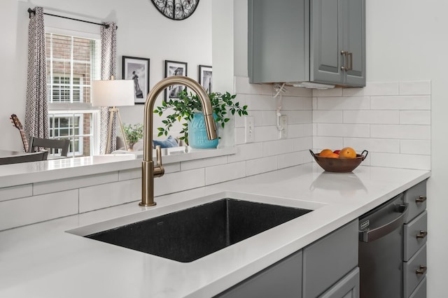 kitchen featuring a sink, dishwasher, light countertops, decorative backsplash, and gray cabinetry