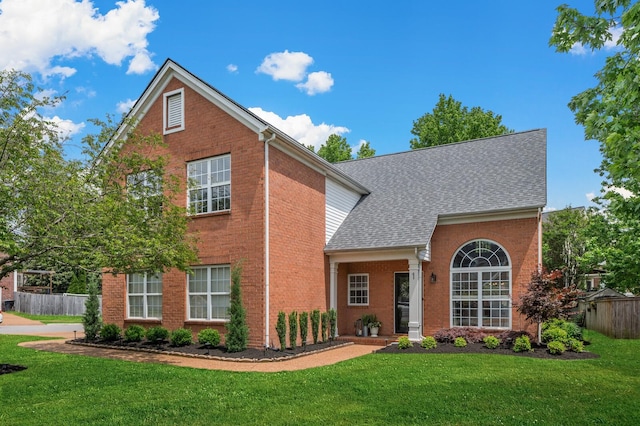 traditional-style house featuring fence, roof with shingles, a front lawn, and brick siding