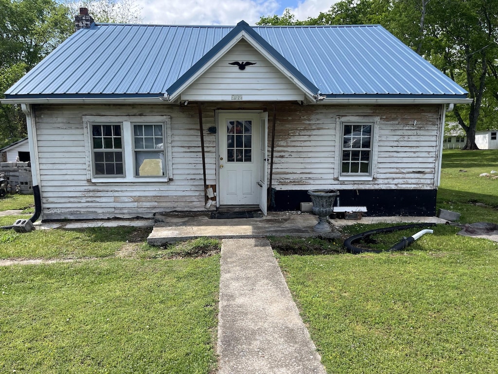 bungalow featuring a chimney, a front yard, and metal roof
