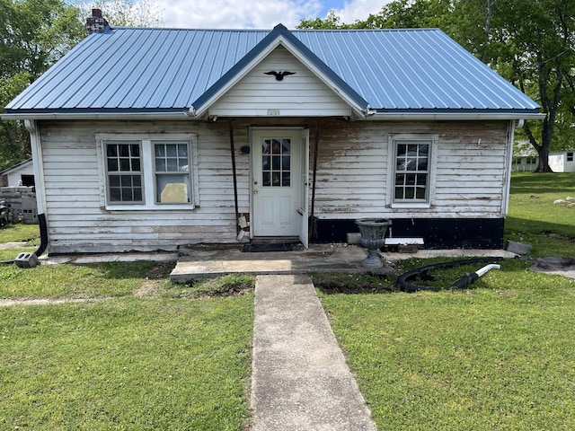 bungalow featuring a chimney, a front yard, and metal roof