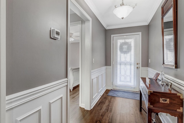 entryway with dark wood finished floors, ornamental molding, and a wainscoted wall