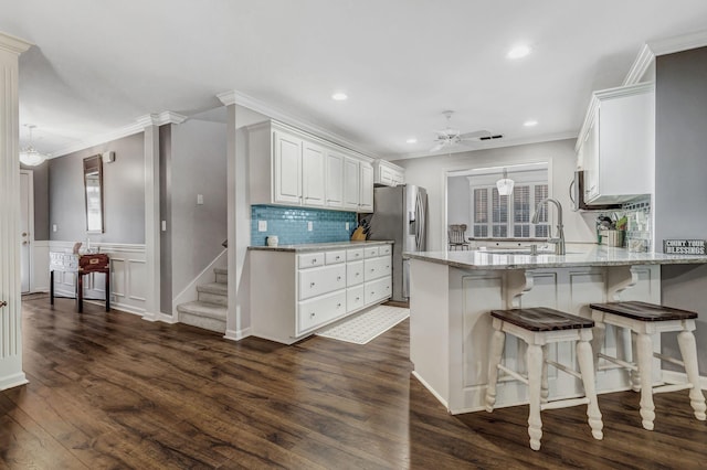 kitchen featuring stainless steel fridge with ice dispenser, ornamental molding, a peninsula, a ceiling fan, and dark wood-style floors