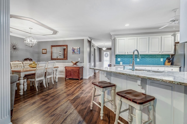kitchen with light stone counters, freestanding refrigerator, ornamental molding, white cabinetry, and dark wood-type flooring
