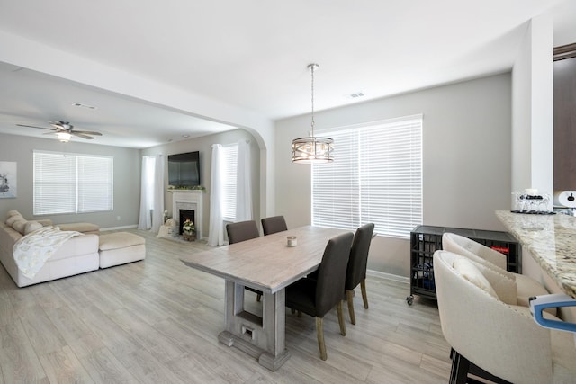 dining space with visible vents, arched walkways, light wood-type flooring, baseboards, and a warm lit fireplace