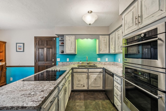 kitchen with a peninsula, a textured ceiling, light stone counters, a sink, and appliances with stainless steel finishes