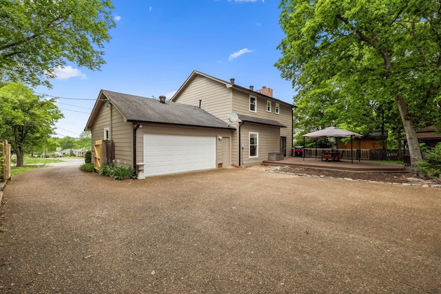 view of side of home featuring a garage, aphalt driveway, a wooden deck, a chimney, and a gazebo