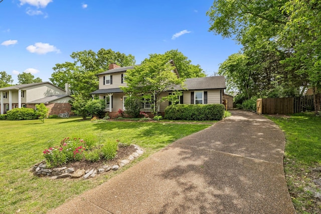 traditional-style home featuring a front lawn, fence, a chimney, and concrete driveway