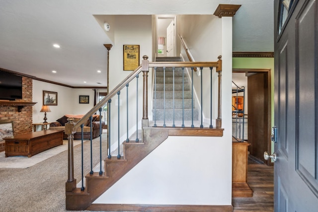 staircase featuring recessed lighting, ornamental molding, a brick fireplace, and wood finished floors