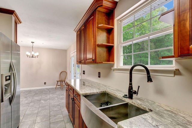 kitchen featuring open shelves, stainless steel refrigerator with ice dispenser, a chandelier, light stone counters, and a sink