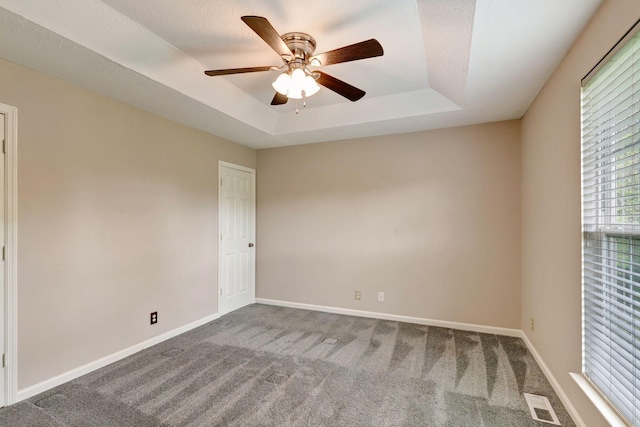 carpeted spare room featuring baseboards, ceiling fan, a tray ceiling, and visible vents